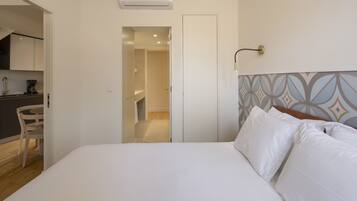 Een hotelkamer met een bed, nachtkastje, stoel, kitchenette en badkamer.