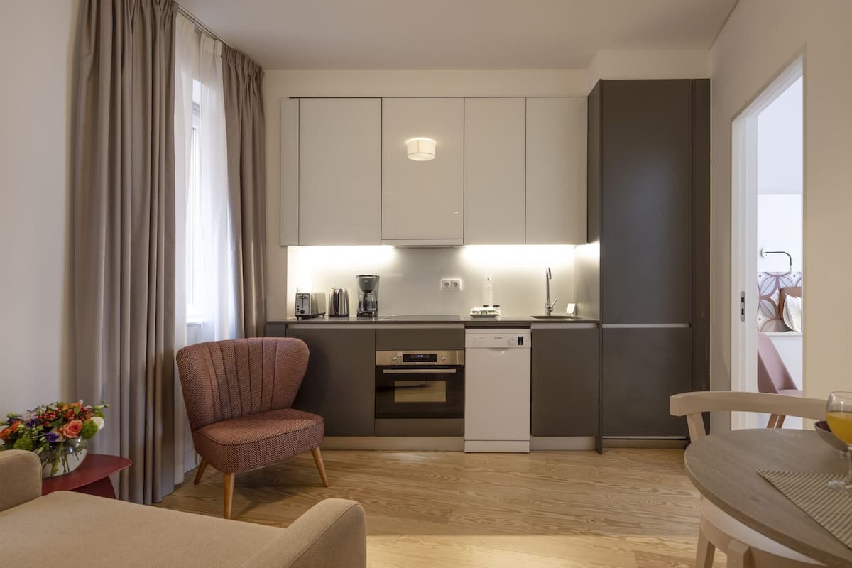 A compact kitchen with modern appliances, a dining area with a table and chairs, and a living space with a sofa and a decorative vase.