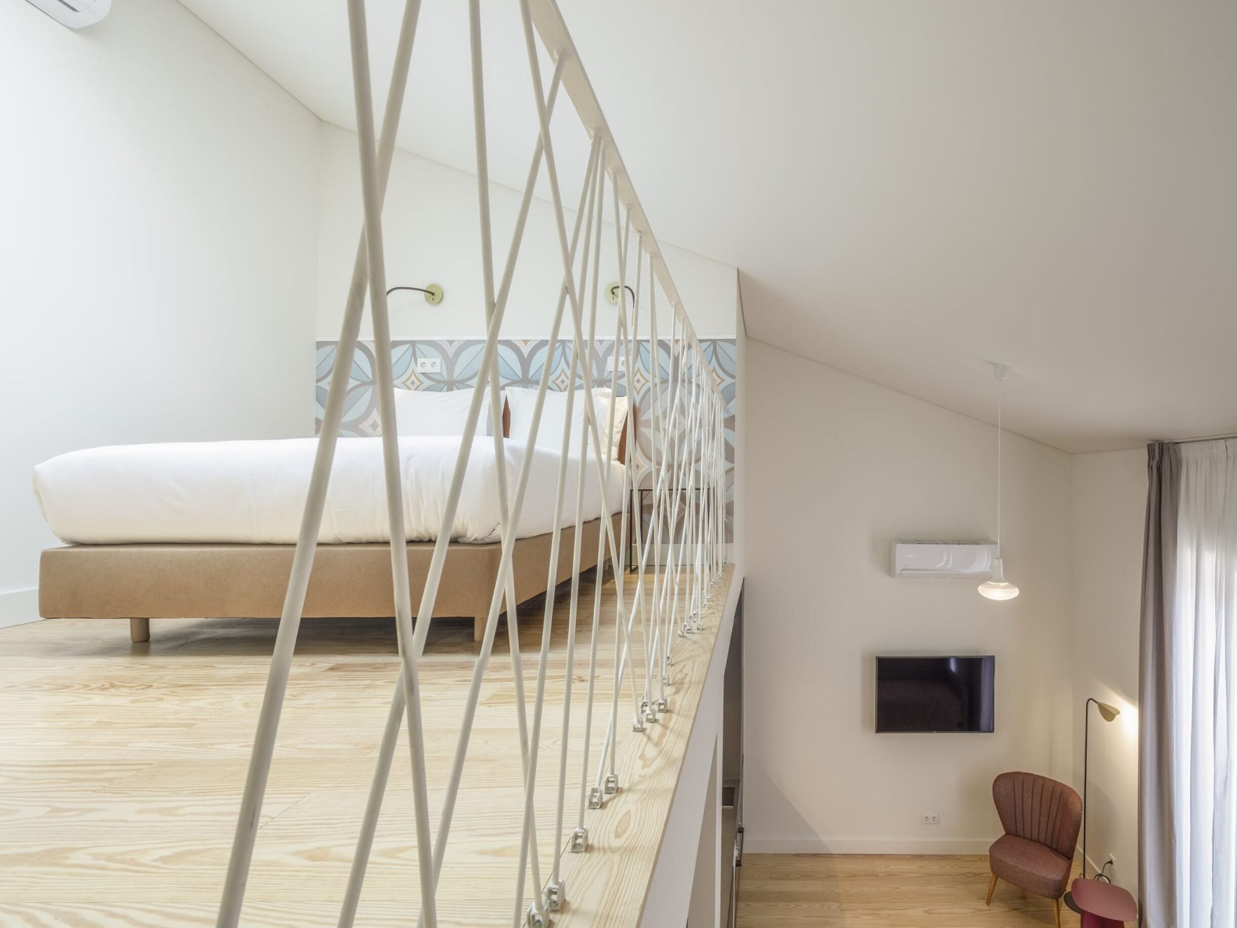 Una camera da letto moderna con un letto, una televisione, una sedia e un'originale struttura con ringhiera bianca.