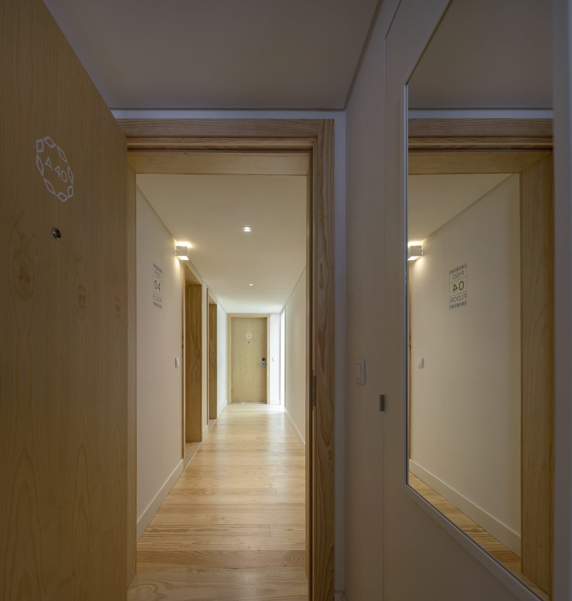 Un pasillo con piso de madera, paredes blancas y puertas con etiquetas que indican los números de habitación y los niveles.