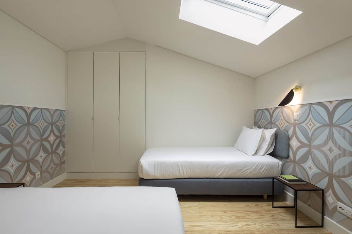 A bedroom with a skylight, a bed, a bedside table, a wardrobe, and patterned wallpaper.
