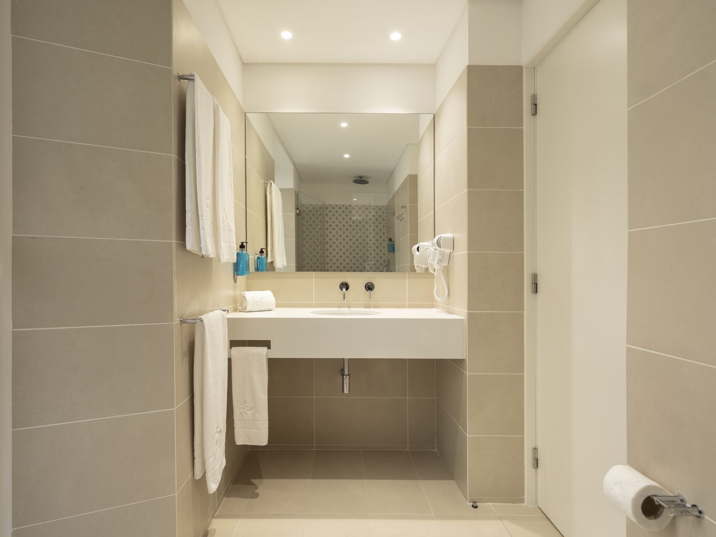 A modern bathroom with a large sink, two mirrors, a towel rack, a hairdryer, and a toilet paper holder.