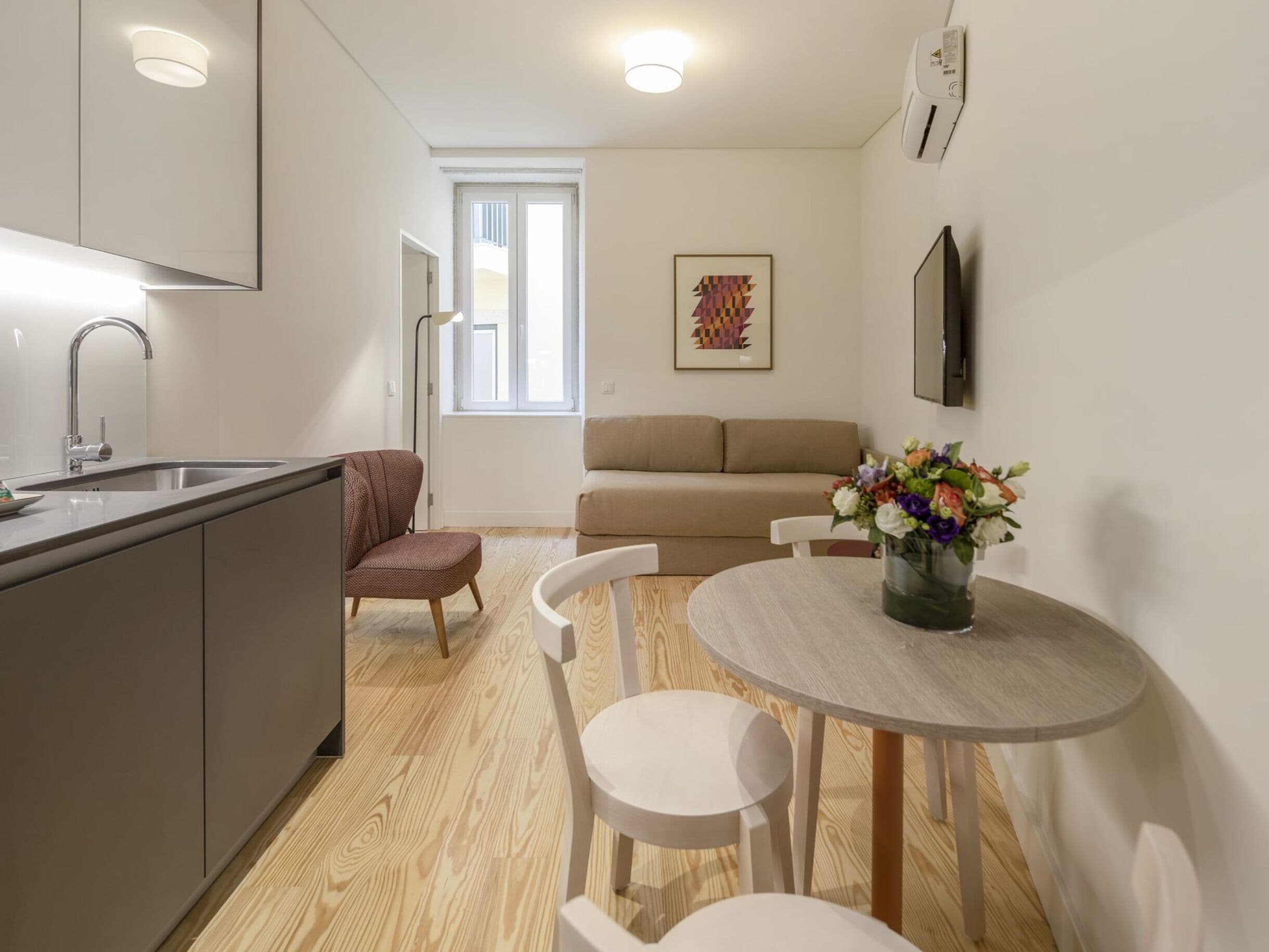 Una cocina moderna con un lavamanos, una silla, una mesa de comedor con sillas, un sofá y un cuadro en la pared.