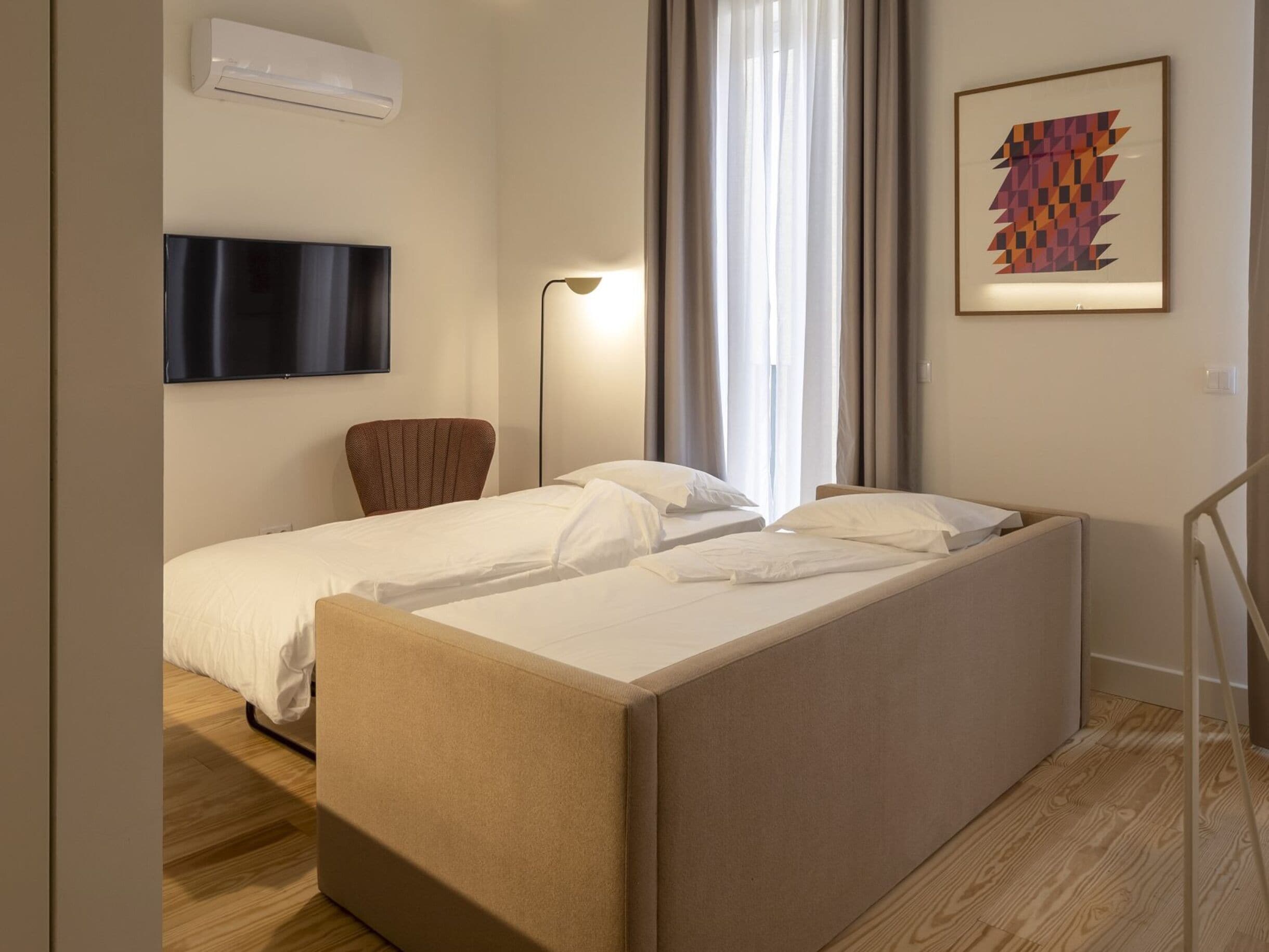 Une chambre d’hôtel avec un lit, une chaise, une télévision, une lampe et un tableau.
