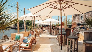 A wooden deck with outdoor seating and umbrellas, overlooking a body of water. - Van der Valk Hotel Mechelen (Mechelen)