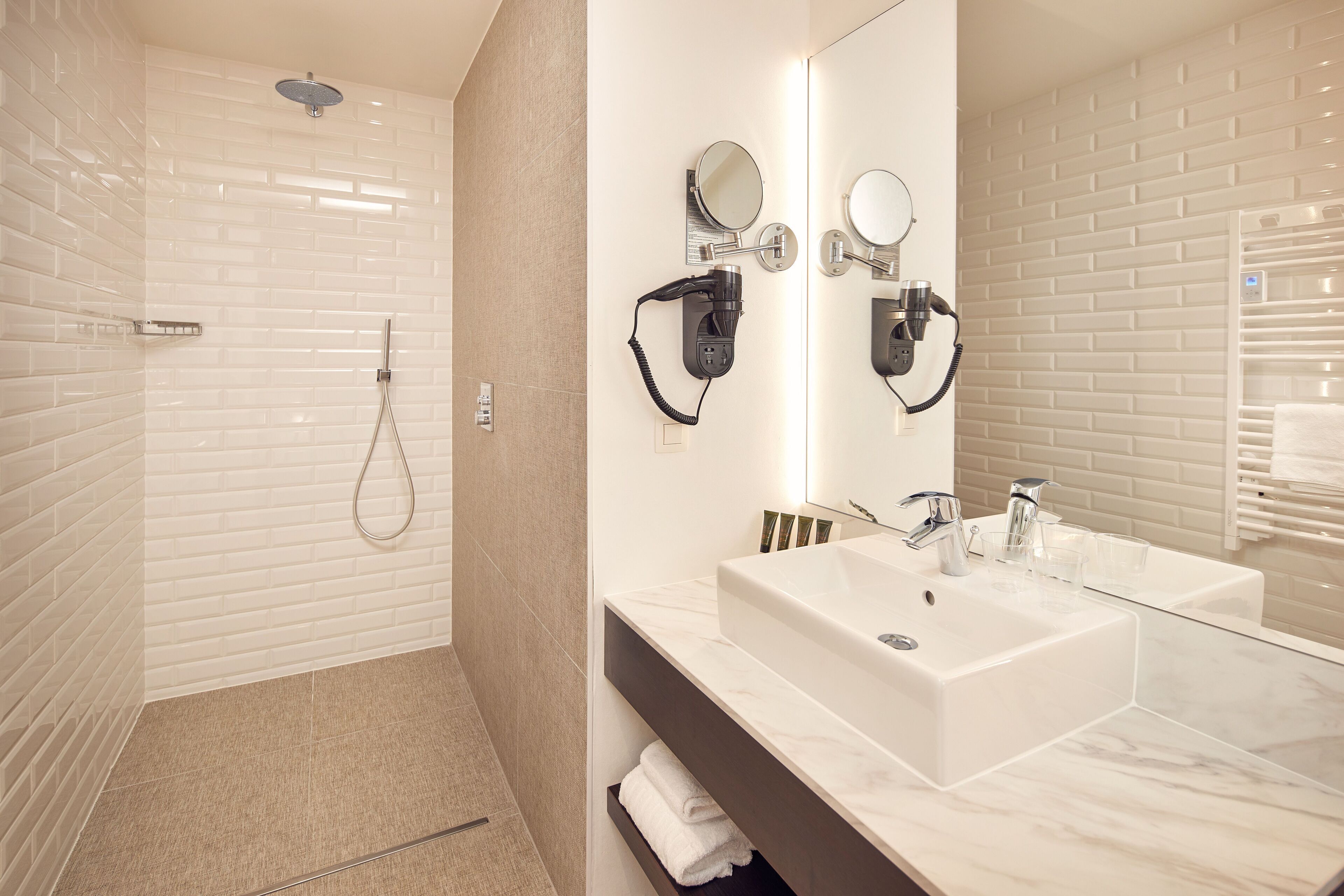 A modern bathroom with a walk-in shower, a large mirror, and a vanity with a sink and towel rack.