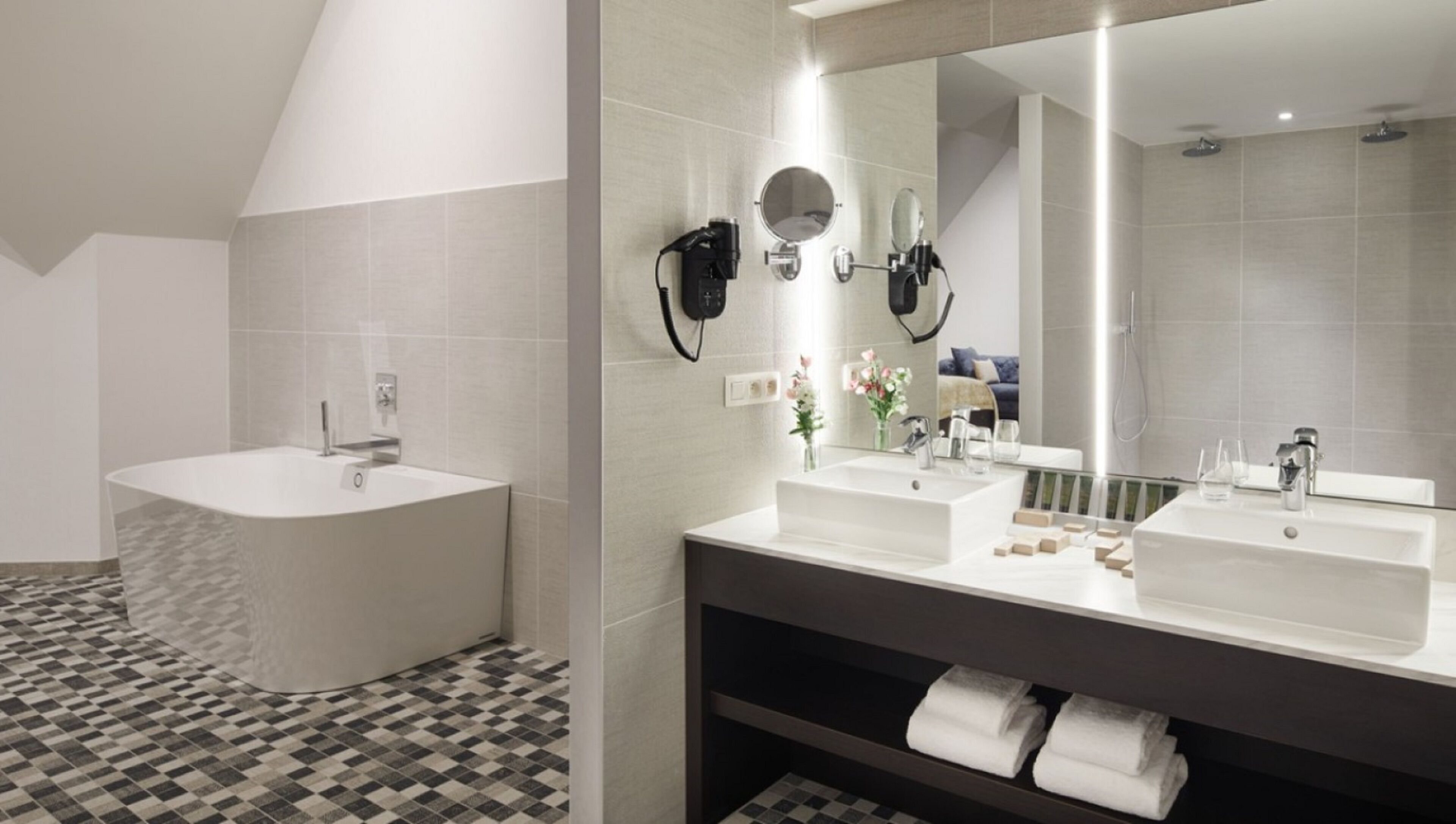 Un baño moderno con una bañera independiente, dos lavamanos, un espejo grande y un perchero para toallas.