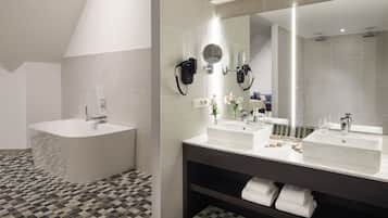 Un baño moderno con una bañera independiente, dos lavamanos, un espejo grande y un perchero para toallas.