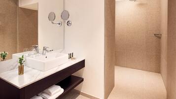 A modern bathroom with a white sink, two mirrors, a shower, and a dark vanity with a towel rack.