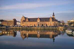 A historic building with a large central tower and multiple smaller towers, reflecting in a calm body of water. - Van der Valk Hotel Mechelen (Mechelen)