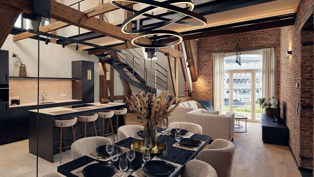 A modern kitchen with a central island, a dining area with a black table set, and a staircase leading to an upper level. - Van der Valk Hotel Mechelen (Mechelen)