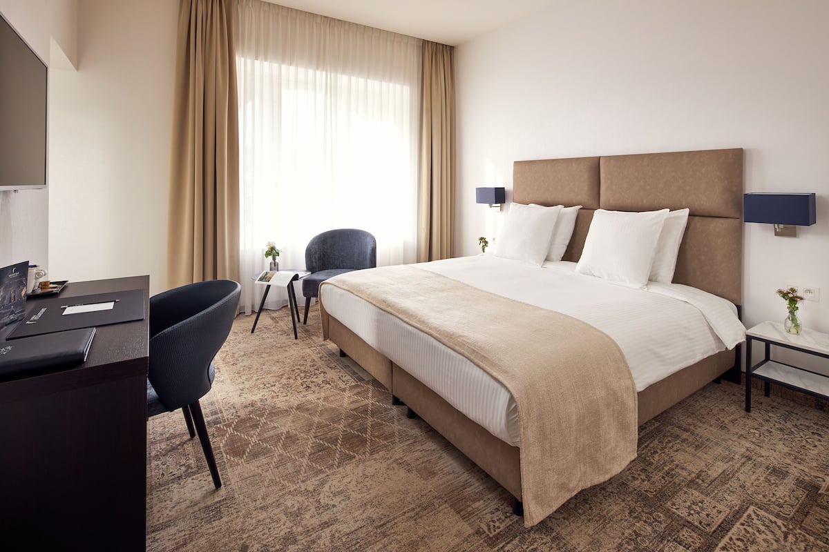 Ein Hotelzimmer mit einem großen Bett, einem Schreibtisch, einem Sessel und einem kleinen Tisch mit einer Vase.