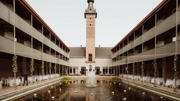 A courtyard with a central fountain, surrounded by tables and chairs, and a tower in the background.