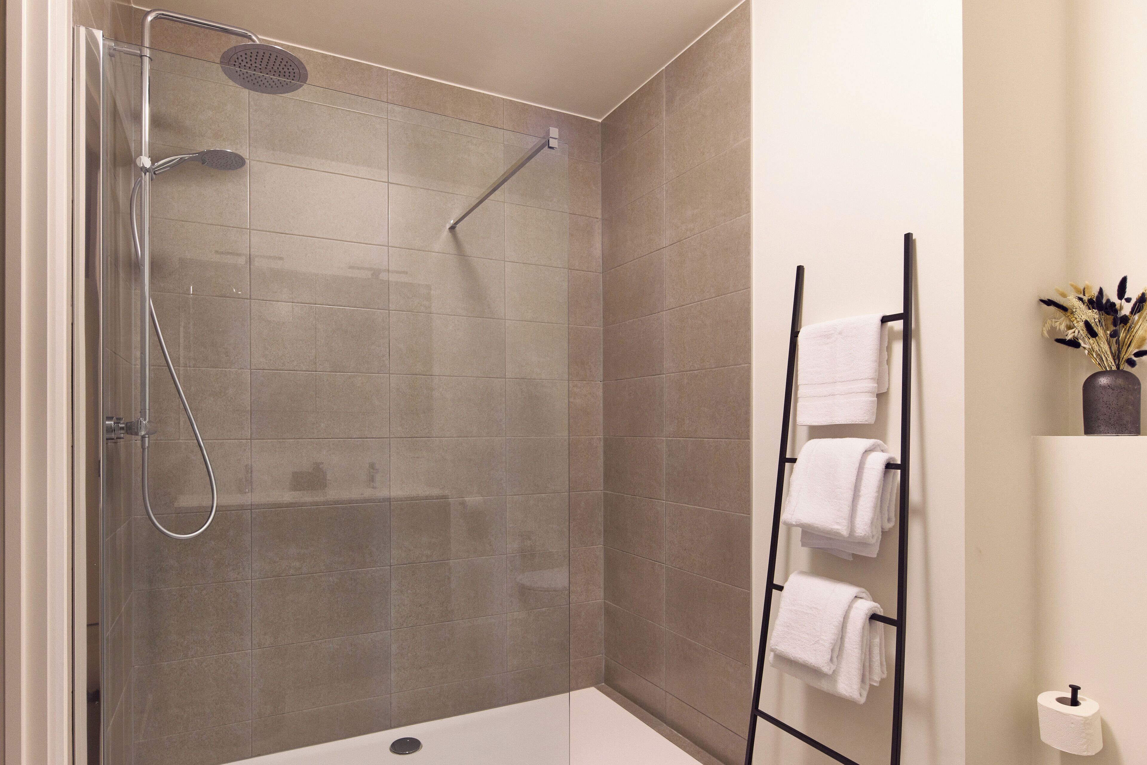 Un baño moderno con ducha de vidrio, un perchero para toallas y un dispensador de papel higiénico.