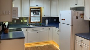 Eine Küche mit weißen Schränken, einem Spülbecken, einem Kühlschrank und einem Fenster mit Jalousien.