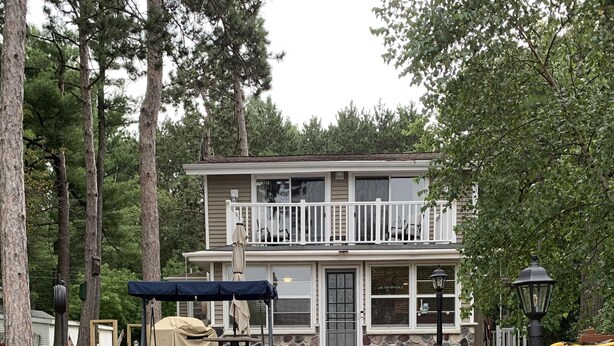 Ein zweistöckiges Haus mit Balkon, Holzterrasse und Garten.