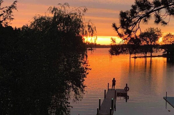 A sunset view from a dock with a calm lake, surrounded by trees. - Private waterfront lake home, Fox Tail Bay, Silver Lake, Wautoma, WI (Wautoma)