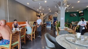 A restaurant with wooden booths, marble tables, and a reception area. - Island Patong Beachfront Apartments (Patong)