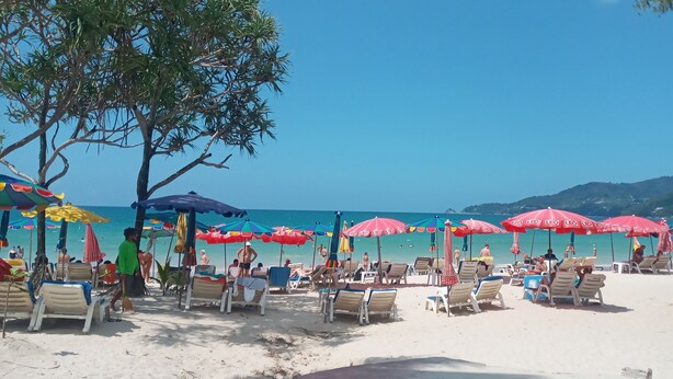 A beach with rows of sun loungers and umbrellas, a clear sky, and a calm sea. - Island Patong Beachfront Apartments (Patong)