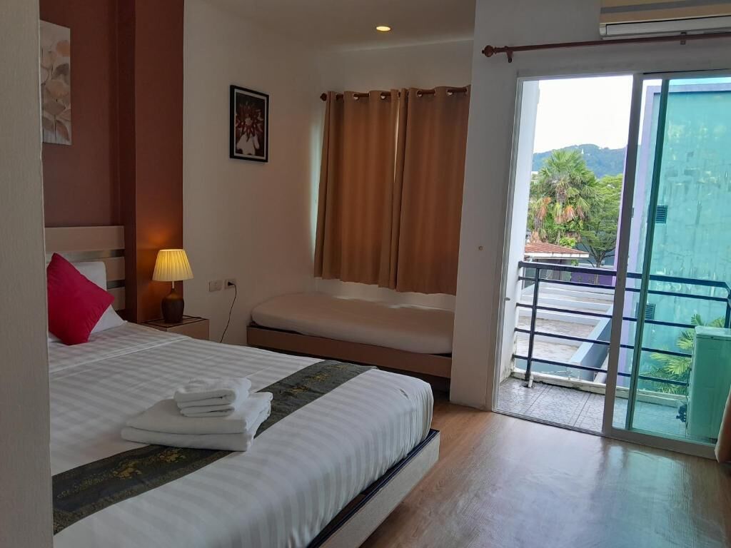 A hotel room with a bed, a bedside lamp, a window with curtains, and a view of greenery outside.