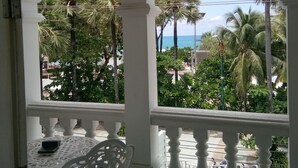 A covered outdoor area with a white balustrade, a white table with a chair, and a view of palm trees and a body of water. - Island Patong Beachfront Apartments (Patong)