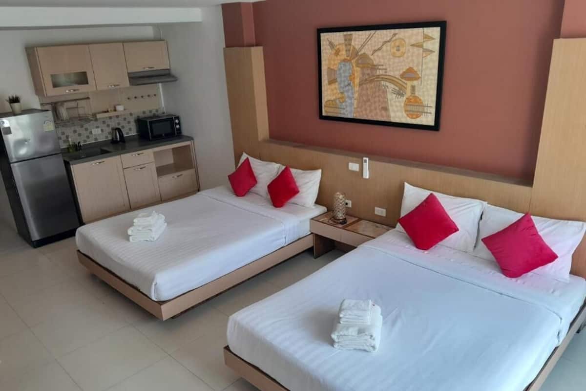 A hotel room with two beds, a kitchenette, and a painting on the wall.
