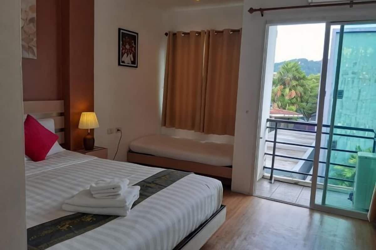 A hotel room with a bed, a nightstand, a lamp, a window with curtains, and a balcony with a view.