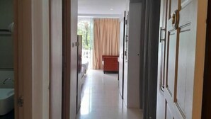 A hallway leading to a bedroom with a bed, a window with curtains, and a bathroom with a sink. - Island Patong Beachfront Apartments (Patong)