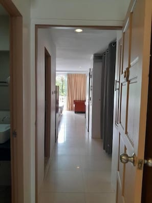 A hallway leading to a bedroom with a bed, a window with curtains, and a bathroom with a sink. - Island Patong Beachfront Apartments (Patong)