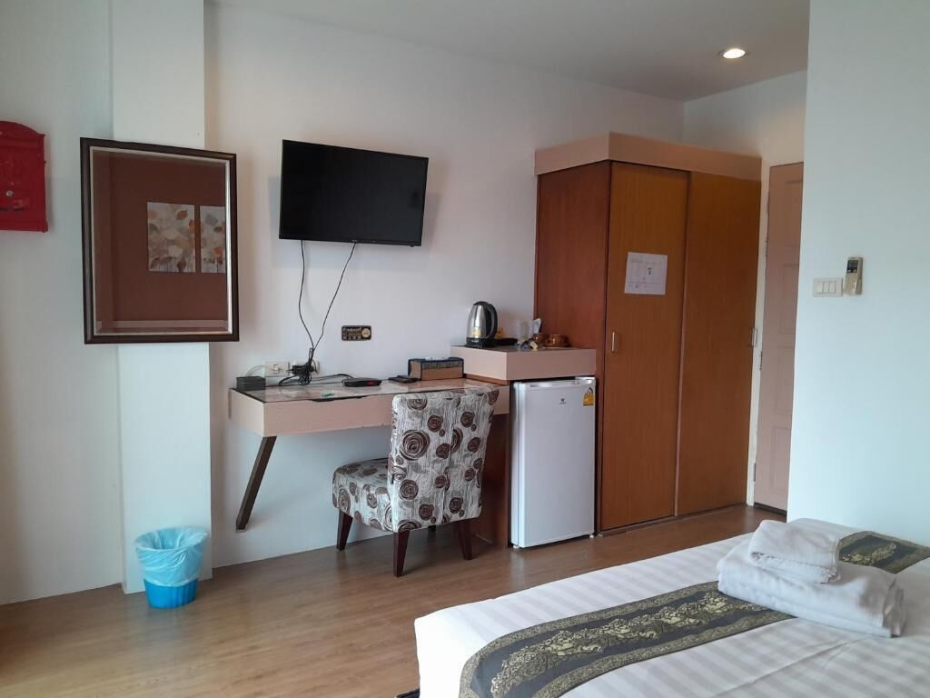 A hotel room with a bed, a desk with a chair, a television, a wardrobe, and a small refrigerator.