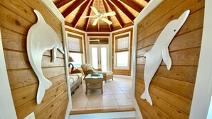 Interior de madera con una escalera que lleva a un balcón, con un ventilador de techo y vigas de madera.