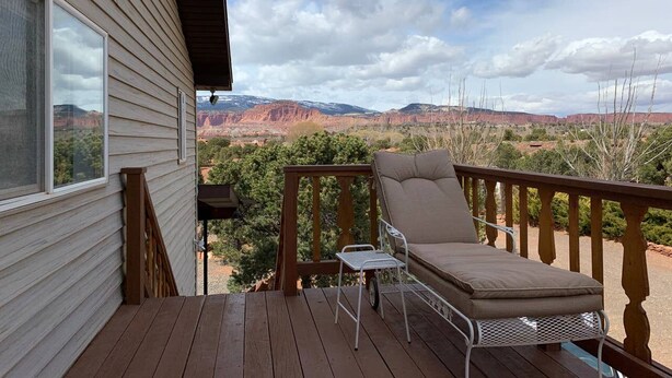 Eine Holzterrasse mit gepolstertem Stuhl und kleinem Tisch, mit Blick auf eine malerische Landschaft mit roten Felsformationen.