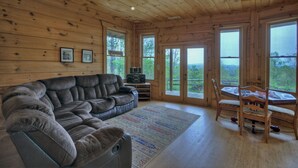 Een houten interieur met een modulaire bank, een eettafel met stoelen en grote ramen met uitzicht op de omgeving.