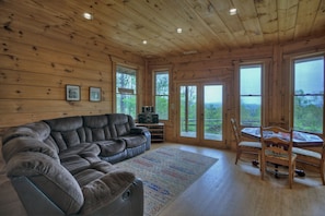 A wooden interior with a sectional sofa, a dining table with chairs, and large windows offering a view of the outdoors. - View From The Top - Aska Adventure Area (Blue Ridge)
