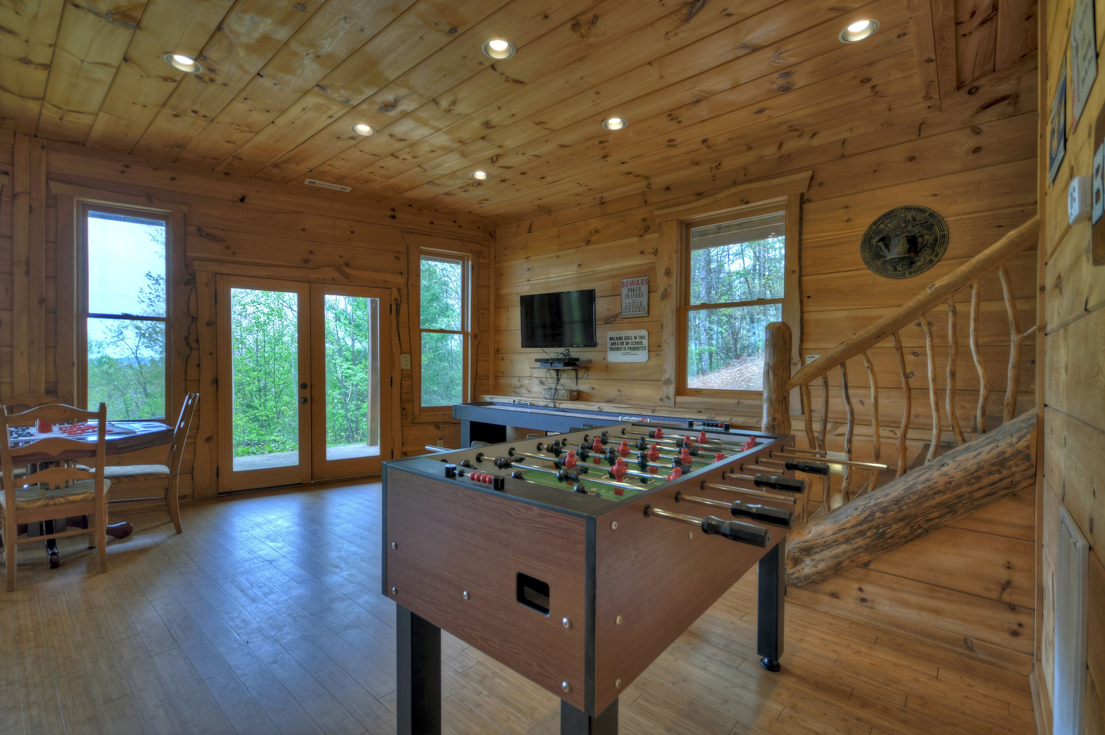 A wooden-floored room with a foosball table, a television, and a staircase.
