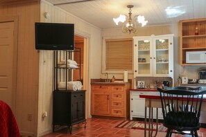 A kitchen with wooden cabinets, a microwave, a sink, and a television mounted above the cabinets.