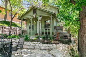 A small, single-story house with a porch, stone steps, and a fenced garden area.