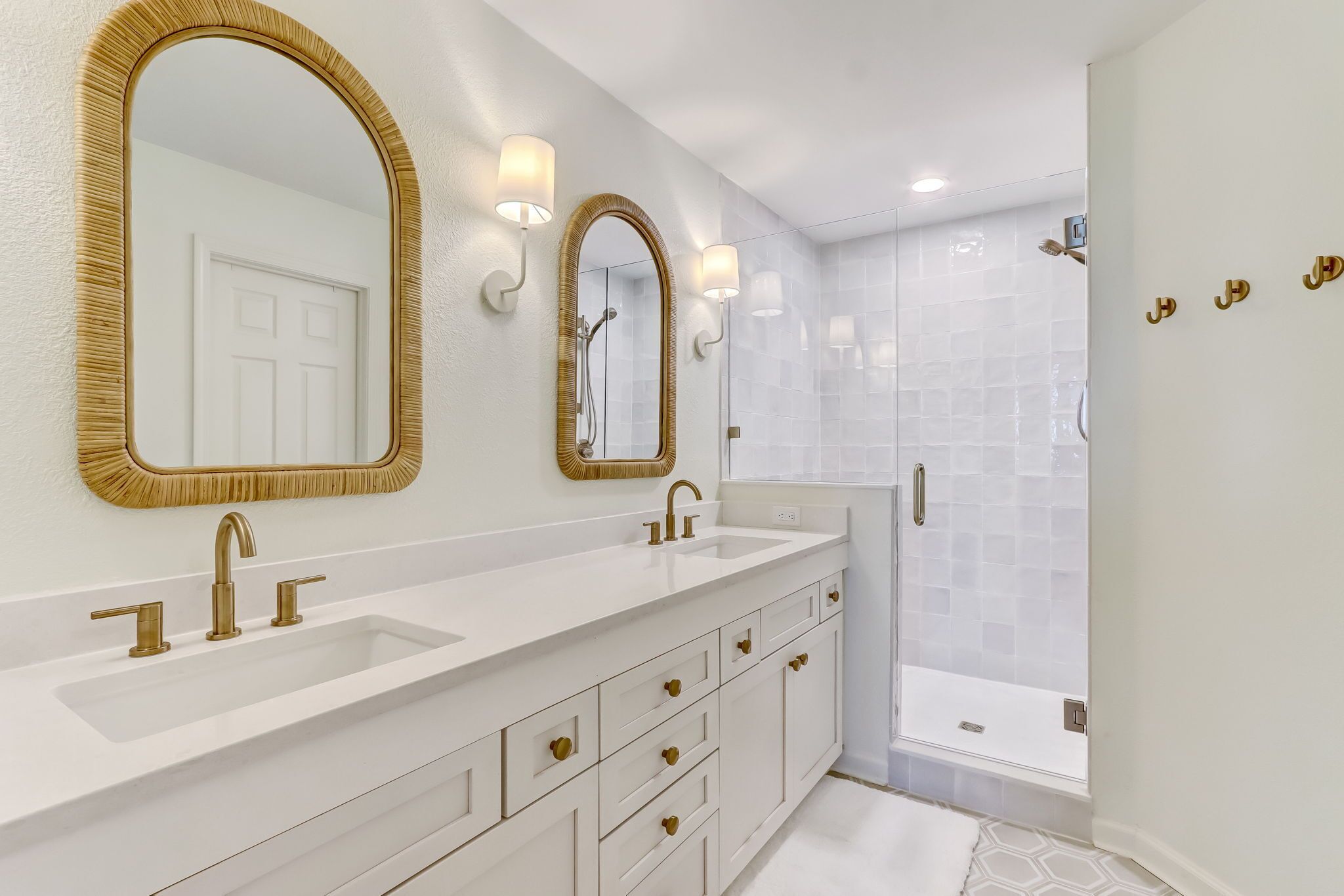A modern bathroom with two sinks, gold-framed mirrors, and a walk-in shower.