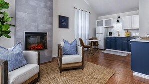 A modern living room with a fireplace, a dining area, and a kitchen with blue cabinets.