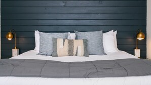A bed with a grey duvet, multiple pillows, and two bedside lamps.