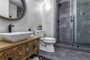 Ein Badezimmer mit einem großzügigen Aufsatzwaschbecken, einer weißen Toilette, einem Holz-Waschtisch und einer Duschkabine aus Glas.