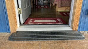 Une porte en bois qui donne sur une pièce où se trouvent un lit, une chaise et un tapis.