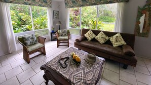 A living room with a brown sofa, two wicker chairs, a patterned table, and a ceiling fan.