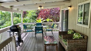 A covered outdoor area with a table and chairs, a grill, and a wicker sofa.