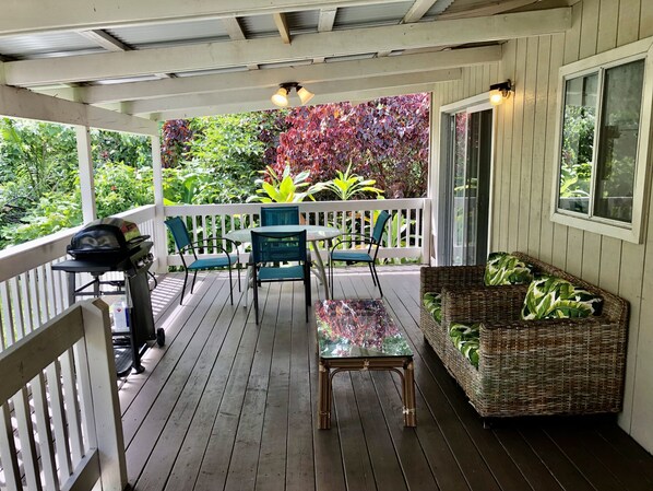 Un espacio al aire libre techado con mesa y sillas, una parrilla y un sofá de mimbre.