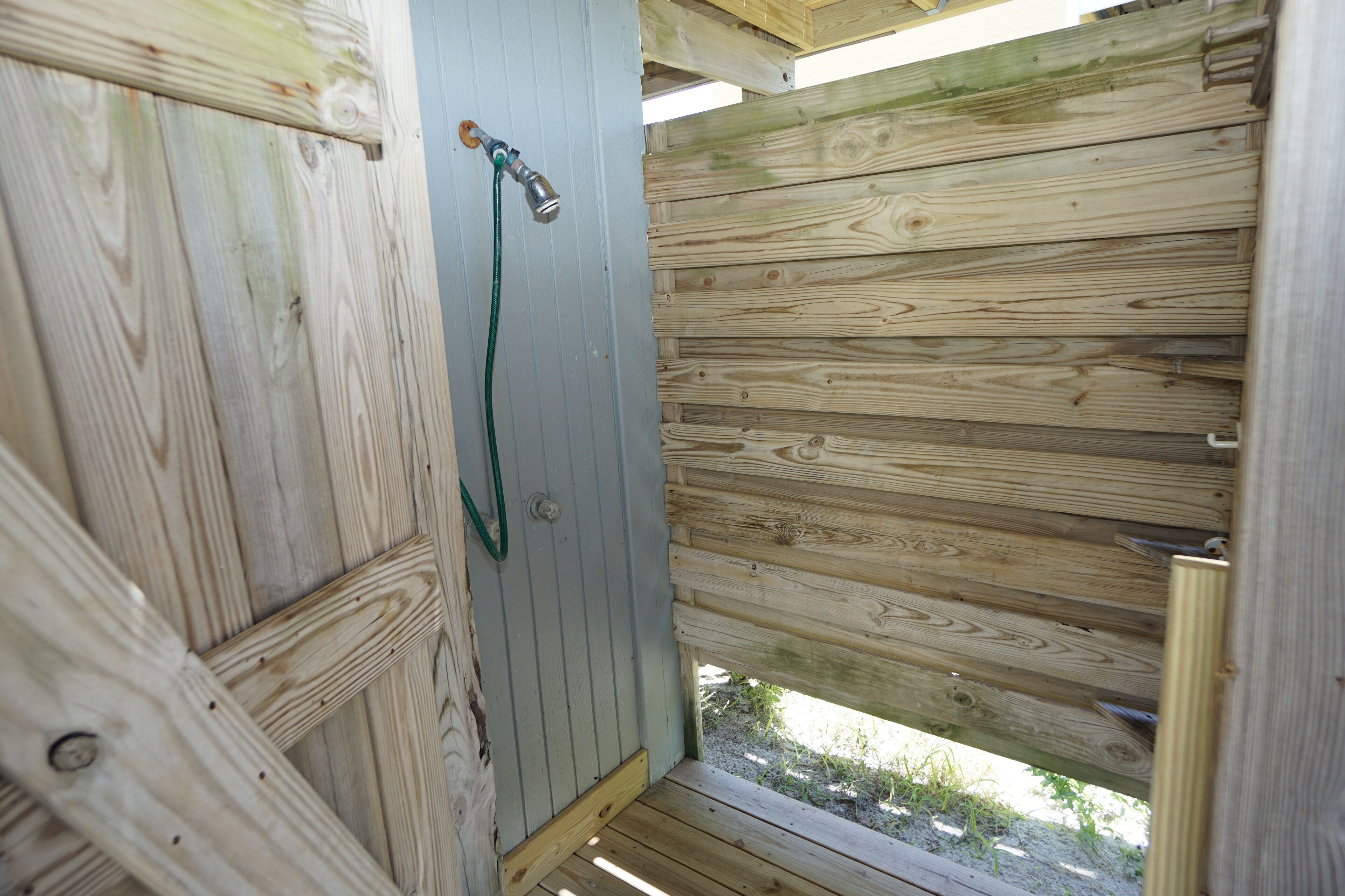 A wooden outdoor shower with a hose and a wooden door.