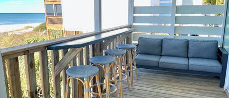 Eine Holzterrasse mit weißer Reling, einem grauen Sofa und vier Weidekorbstühlen.