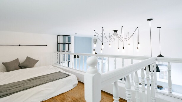 Een slaapkamer met een bed, een witte balustrade en uitzicht op de stad.