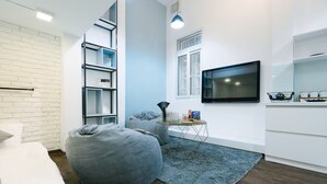 Een moderne kamer met een bed, een grijze pluchen zitbal, een televisie en een boekenkast.