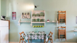 A small kitchen with a dining table, chairs, a coffee maker, and shelves with dishes and cups. - St Spyridon Cosy Apartment By Konnect (Corfu)
